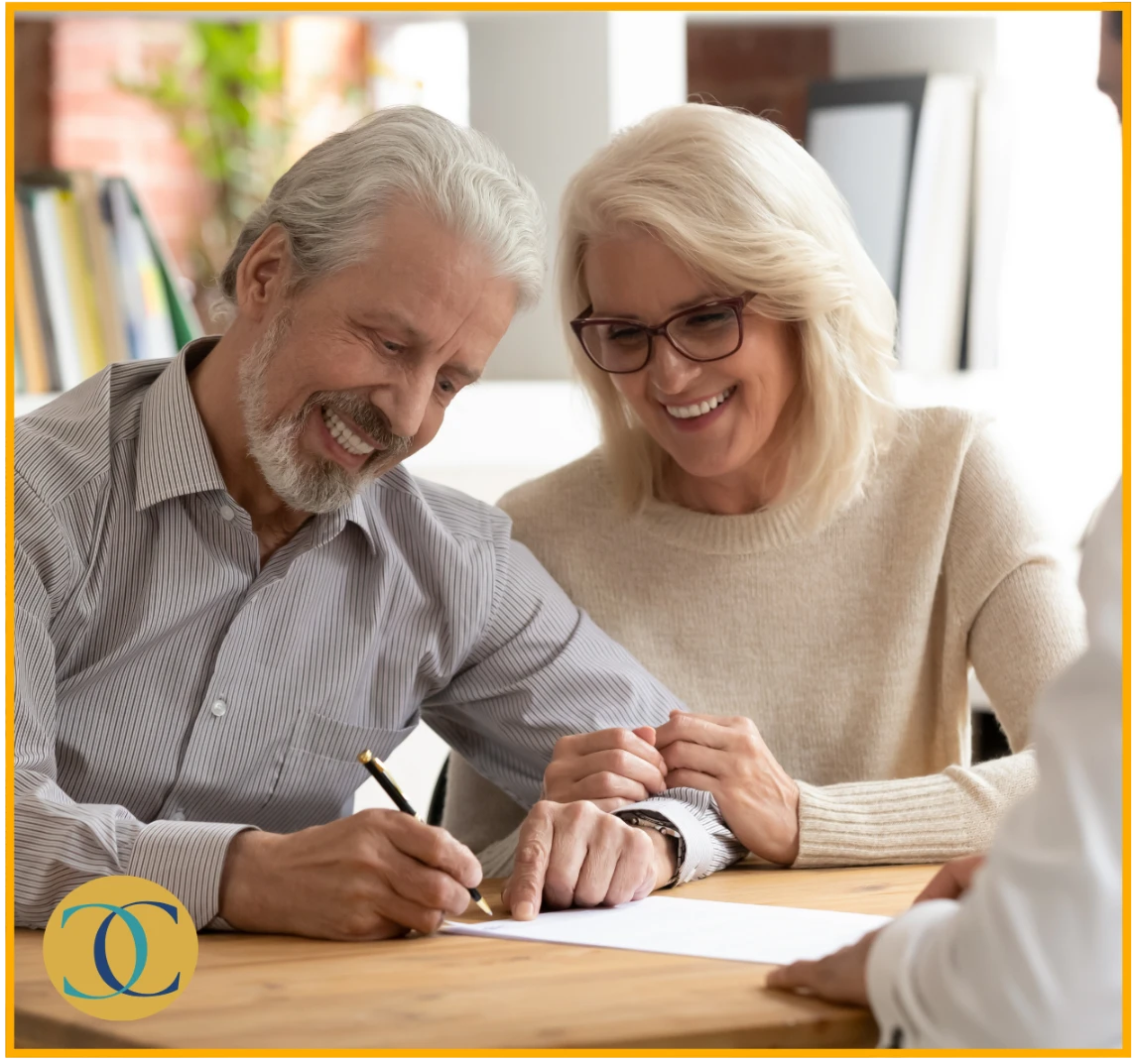 An elderly couple smiling and signing a document together, with one of them holding a pen and the other pointing at the paper. Chirosconnect