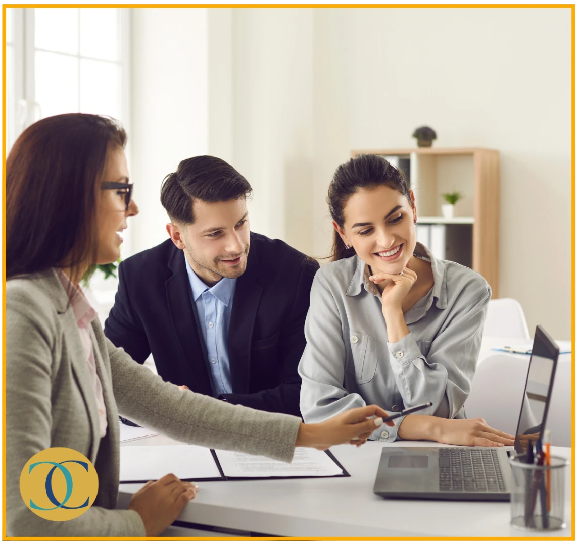 Three professionals in a meeting, smiling and discussing something on a laptop. Two are seated, while one is pointing at the screen. Chirosconnect
